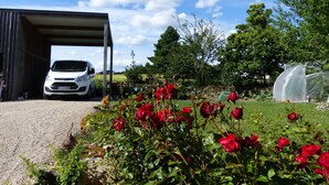 A white car parked under a covered area with a gravel path leading to it.
