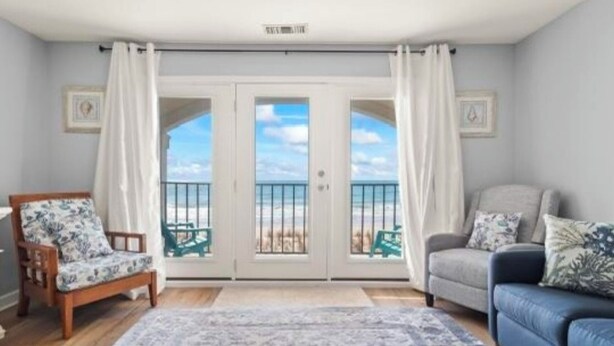 Ein Zimmer mit Balkon, einem Holzstuhl, einem blauen Sofa und einem gemusterten Teppich.