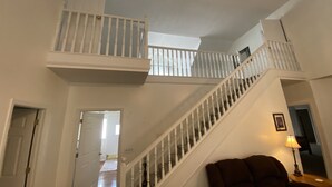 Un intérieur à plusieurs niveaux, avec un escalier, une porte donnant sur une autre pièce et une lampe sur une table d’appoint.