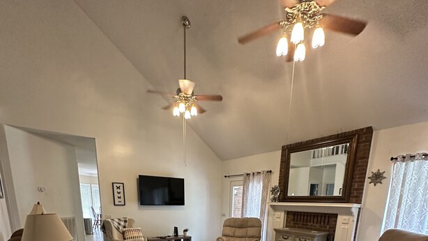Un salon spacieux doté d’un ventilateur de plafond, d’une cheminée et d’un téléviseur fixé au mur.