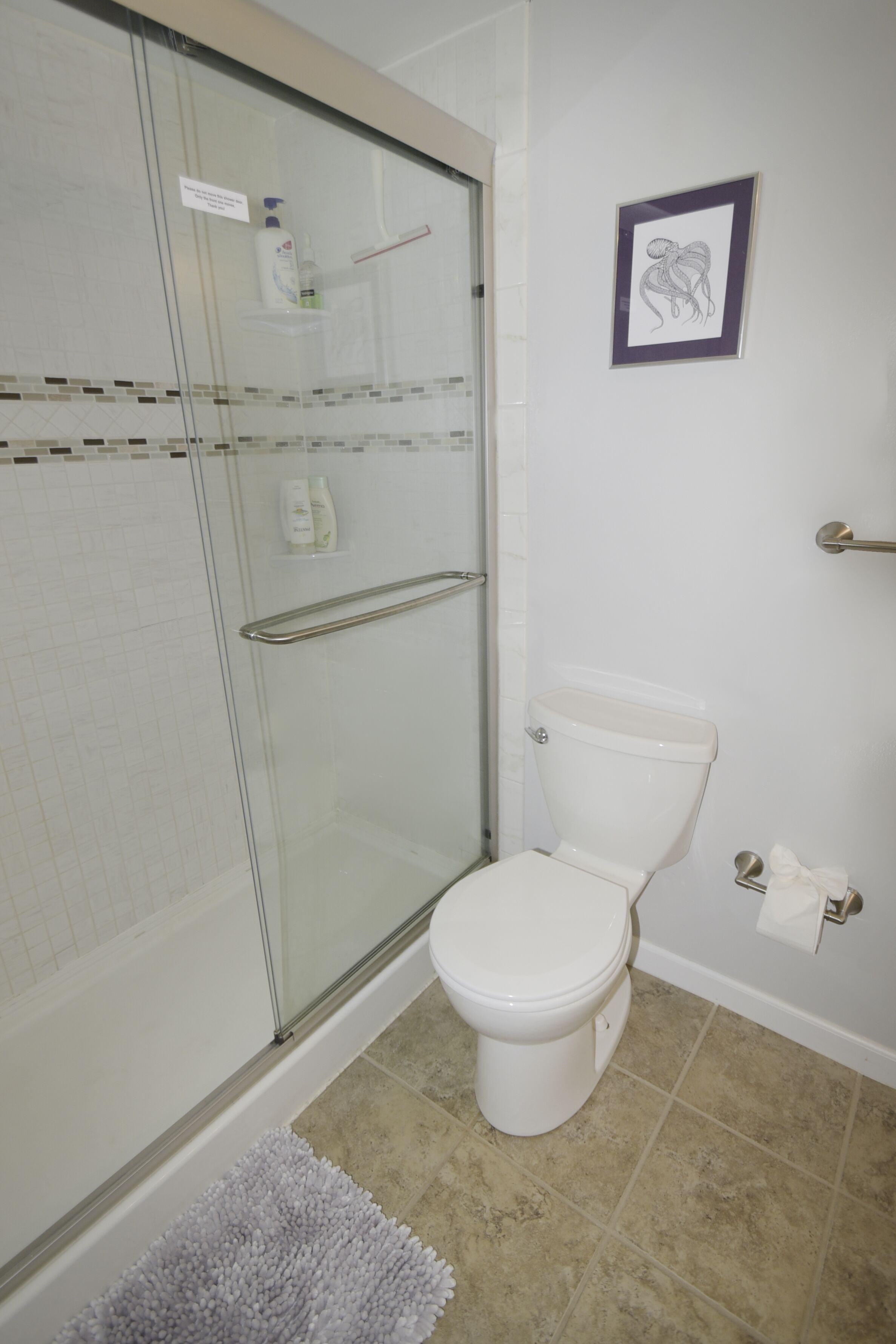 A bathroom with a glass shower enclosure, a white toilet, and a framed picture on the wall.