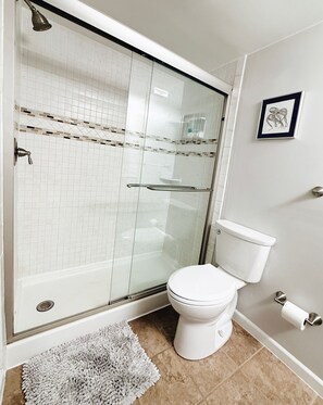 Une salle de bain avec une douche à parois de verre, des toilettes et un tableau encadré au mur.