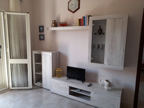 Una sala de estar moderna con televisor empotrado, estantería y aparador con puertas de cristal.