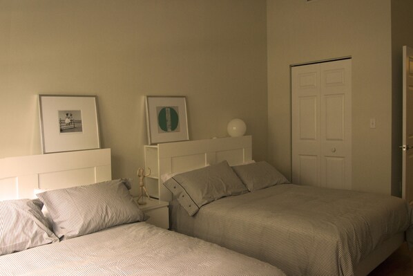 A bedroom with two beds, a white headboard, a door, and framed pictures on the wall. - BEACHFRONT LUXURIOUS CONDO (Hallandale Beach)