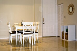 A dining area with a white table and chairs, a white door, and a small shelf with decorative items. - BEACHFRONT LUXURIOUS CONDO (Hallandale Beach)