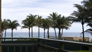 Blick auf einen Balkon mit Geländer, Palmen und dem Meer im Hintergrund.