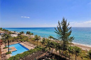 A resort with a swimming pool, beach, and palm trees. - BEACHFRONT LUXURIOUS CONDO (Hallandale Beach)
