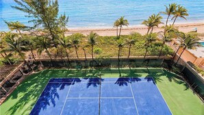 Ein Tennisplatz mit Blick auf den Strand und Palmen.