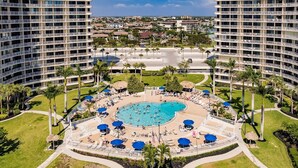 Um hotel com piscina central rodeada por espreguiçadeiras e guarda-sóis, oferecendo vista da região circundante.