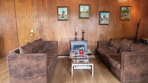 Un salon avec deux canapés marron, une table basse en verre et des murs recouverts de panneaux en bois, ornés de trois tableaux encadrés.