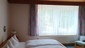 Une pièce avec un plafond en bois, un lit avec une literie blanche, une table de chevet, une lampe, une fenêtre avec des rideaux et un radiateur.