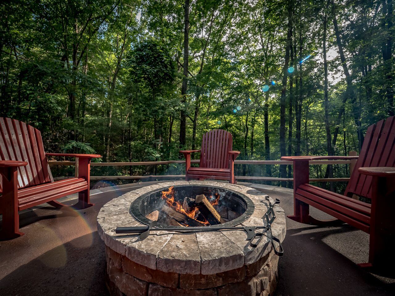 A circular fire pit with seating around it, surrounded by a forested area.