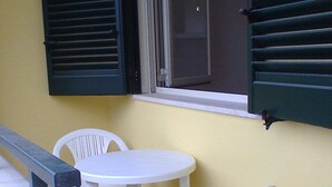 A small outdoor seating area with a table and two chairs, a bench, and a window with green shutters. - "LE SORELLE" holiday home with sea view Santa Maria al Bagno 100 meters from the beach (Nardò)