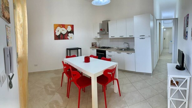 A modern kitchen with white cabinets, a dining table with red chairs, and a painting on the wall. - "LE SORELLE" holiday home with sea view Santa Maria al Bagno 100 meters from the beach (Nardò)