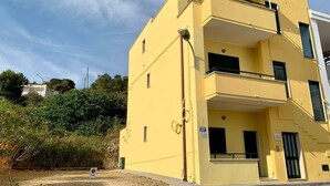A yellow multi-story building with a balcony on the second floor, a door with a sign, and a small window on the ground floor. - "LE SORELLE" holiday home with sea view Santa Maria al Bagno 100 meters from the beach (Nardò)