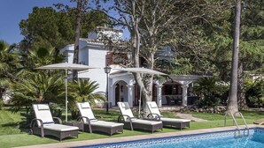 A poolside area with lounge chairs and umbrellas, a white building with arches, and a clear blue pool.