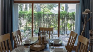 A dining area with a table set for four, large windows with curtains, and a view of greenery outside.