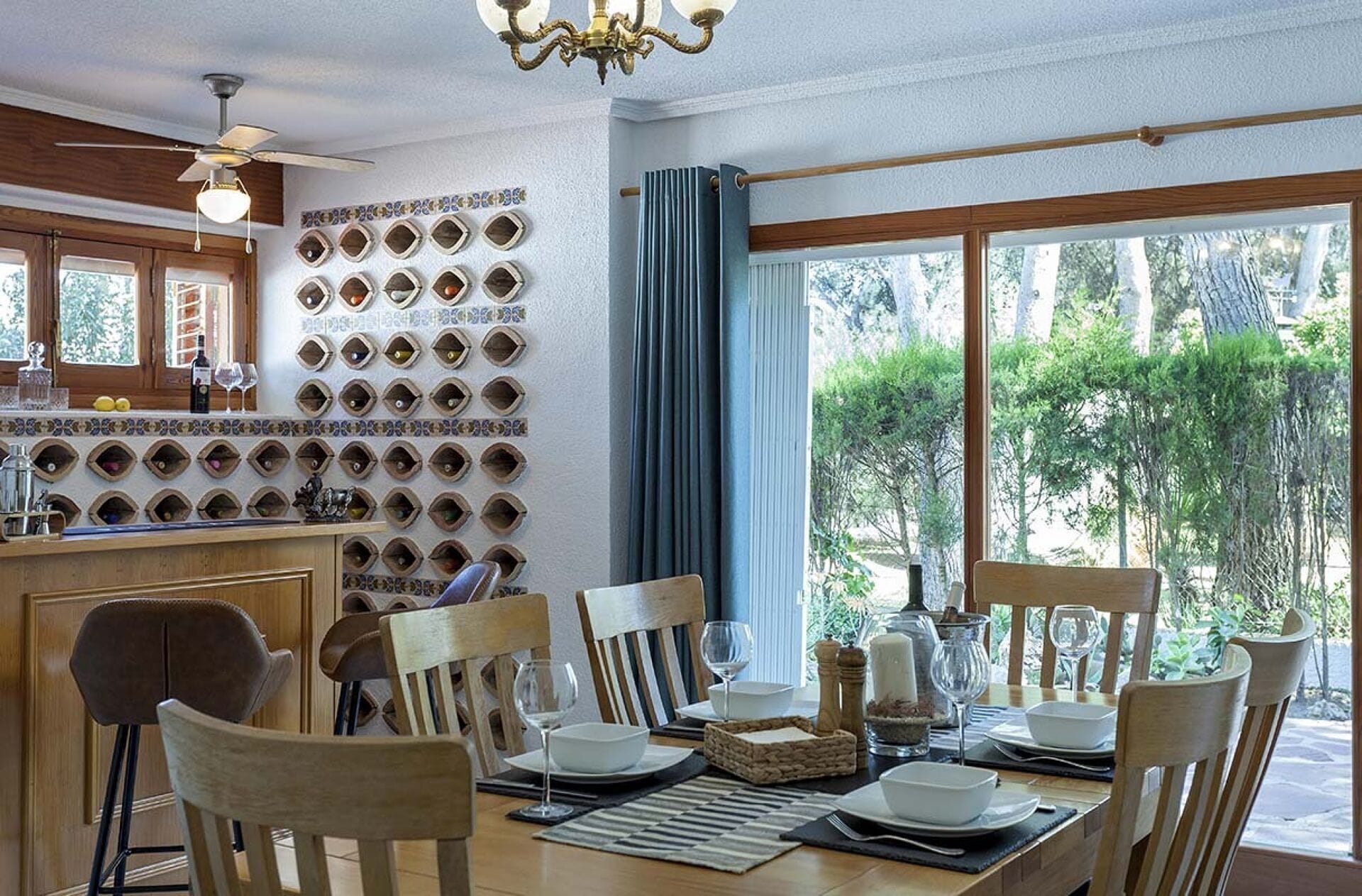 Comedor con una pared de botellas de vino, un candelabro y vistas a la vegetación.