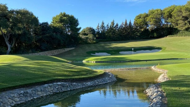 Un campo de golf con un estanque, árboles y cielo despejado.