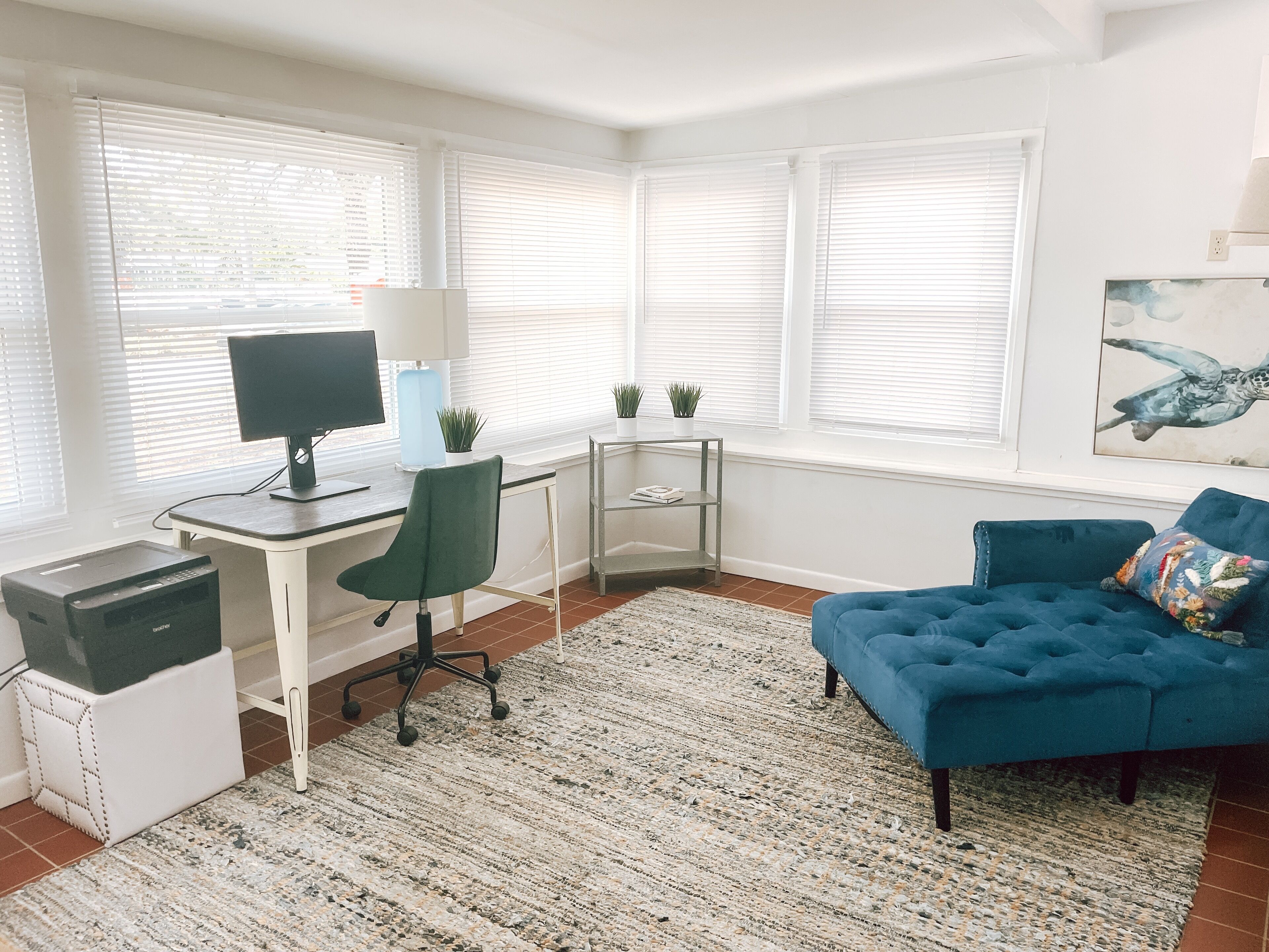 A modern living room with a desk, a blue sofa, and a painting on the wall.