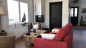 A living room with a red sofa, a wooden coffee table, a wicker chair, a television, and a black door. - Rental House Quiberon 6 beds (Quiberon)