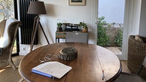 A round wooden table with a notebook, a pen, and a pair of earphones. There are two wicker chairs, a lamp, and a small wooden table with plants and a scale. Two framed pictures hang on the wall. - Rental House Quiberon 6 beds (Quiberon)