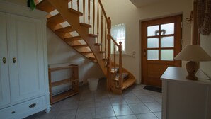 A staircase leading to an upper floor, a white cabinet, a wooden door with frosted glass panels, and a lamp on a table.