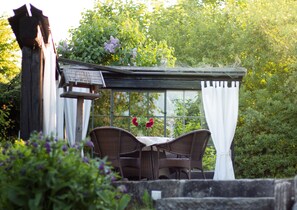 A conservatory with wicker furniture and a table, surrounded by greenery and flowers. - Lovingly furnished, cozy cottage in country style. (Oybin)