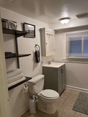 A bathroom with a toilet, sink, towel rack, and a window with blinds. - Comfy Garden Suite in Andersonville (Chicago)