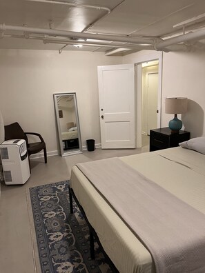 A bedroom with a bed, a chair, a desk, a lamp, a mirror, and a radiator. - Comfy Garden Suite in Andersonville (Chicago)