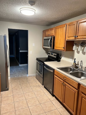 A kitchen with wooden cabinets, a stainless steel refrigerator, a microwave, an oven, and a dishwasher.