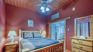 Une chambre à coucher avec un lit en bois, deux tables de chevet, une commode, une coiffeuse et un ventilateur de plafond.