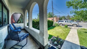 Une terrasse couverte avec deux chaises longues, un chemin en béton et une vue sur une rue où sont garées des voitures, ainsi que sur un immeuble.