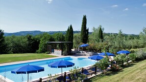 Una piscina con sombrillas azules, rodeada de vegetación y colinas al fondo.