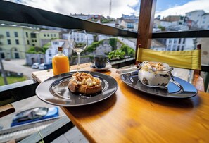 A dining table with a meal, a glass of orange juice, and a view of buildings through a window. - Hotel A. G. Porcillán (Ribadeo)