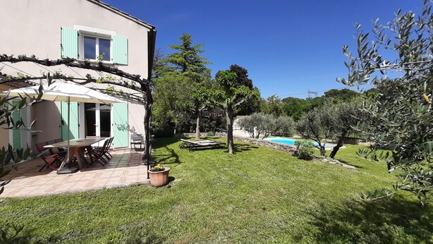 Una casa con patio, piscina y jardín con árboles y césped.