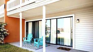 Un espace extérieur abrité, doté de deux chaises turquoise et d’un tapis à motifs, situé à côté d’une porte-fenêtre coulissante donnant sur un balcon.