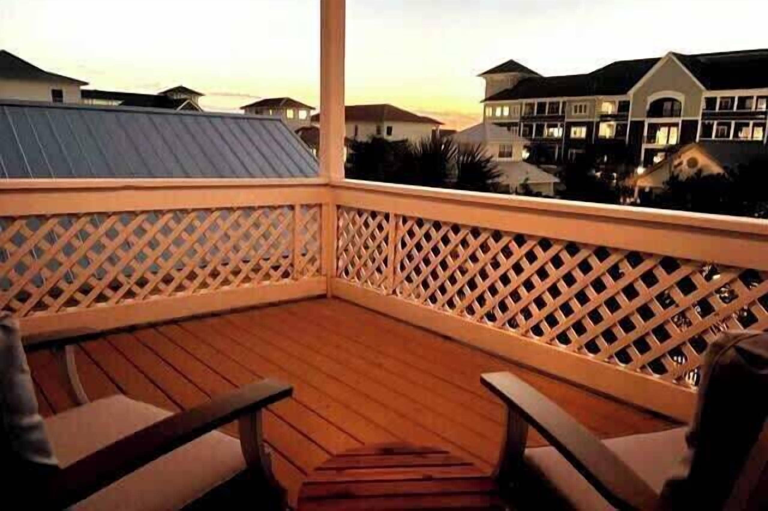 Een houten terras met een spijlenhek, houten stoelen en uitzicht op woonhuizen op de achtergrond.