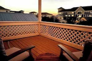 A wooden deck with a lattice railing, wooden chairs, and a view of residential buildings in the background.
