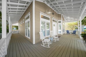 A covered porch with a wooden deck, white railings, and two rocking chairs. - Timeless Traditions-Golf Cart Deals-Steps to Beach (Destin)