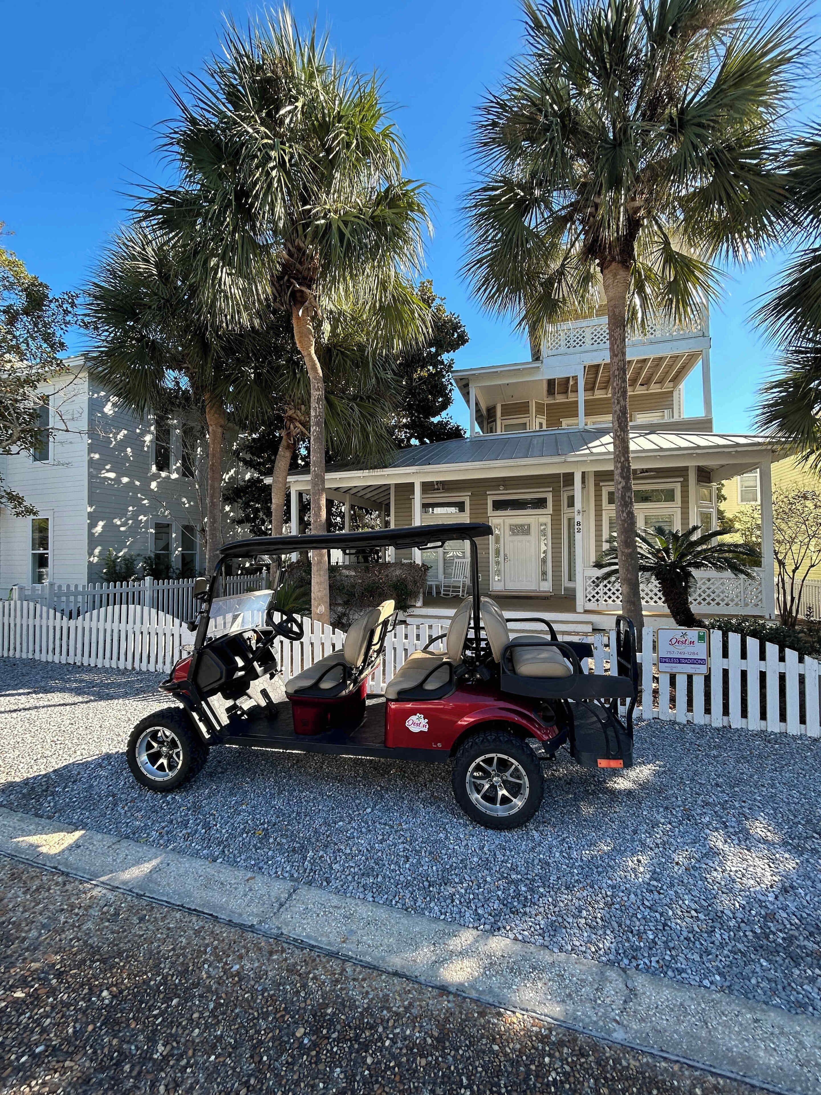 A golf cart parked in front of a building with a white picket fence, palm trees, and a clear blue sky.