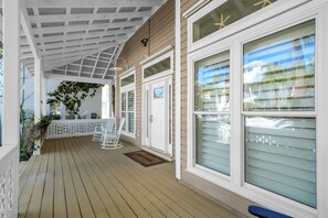 A covered porch with a wooden deck, white railings, and a door with a window.
