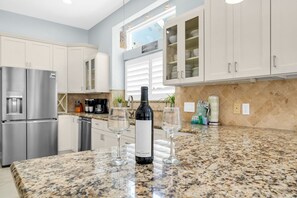 A kitchen with granite countertops, stainless steel appliances, and a wine bottle. - Timeless Traditions-Golf Cart Deals-Steps to Beach (Destin)