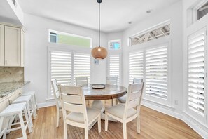 A dining area with a round table, white chairs, and a hanging light fixture.