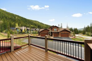 A residential area with a wooden deck, houses with brown roofs, and a forested hillside in the background.