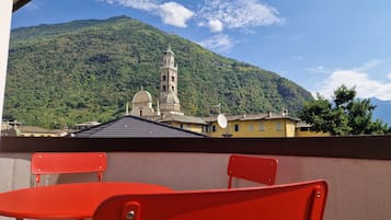 Un balcon avec des chaises rouges donnant sur une montagne où se trouvent une église et un clocher.