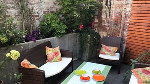 Une terrasse dotée de meubles en osier, d’une table recouverte d’une nappe et agrémentée de différentes plantes.