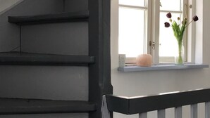 Un escalier avec des rampes noires et des murs blancs, menant à un palier doté d’une fenêtre et d’un vase de fleurs.