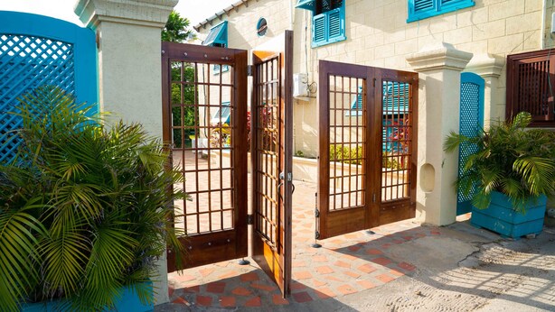 A gated entrance with a tiled pathway leading to a building with blue shutters and a white facade.