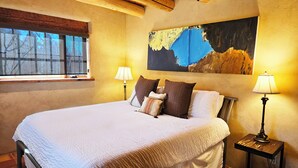 Un dormitorio con una cama grande, dos lámparas de noche, una ventana y un cuadro en la pared.